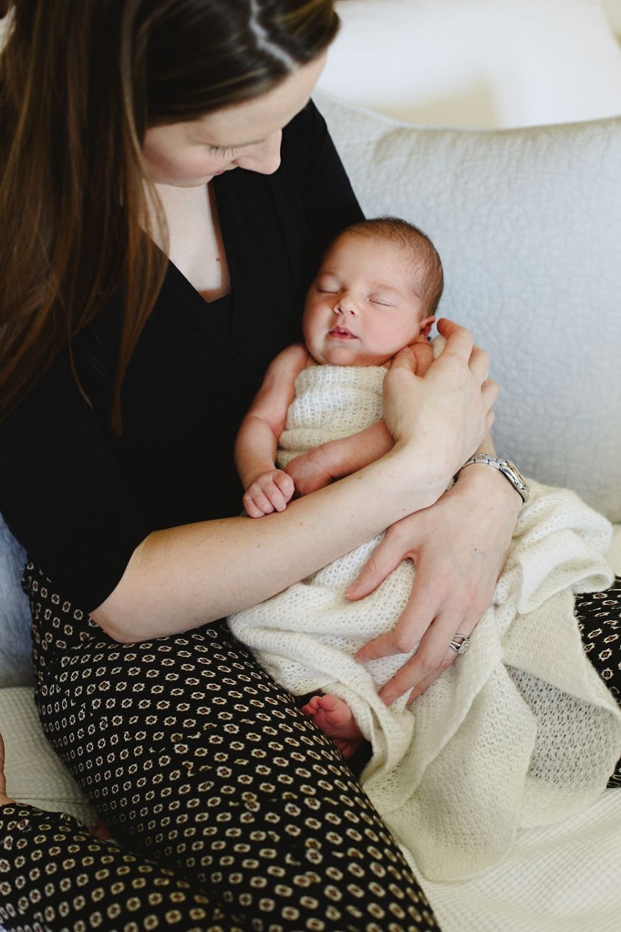 A peaceful newborn baby in cream knitwear sleeps contentedly in gentle arms.