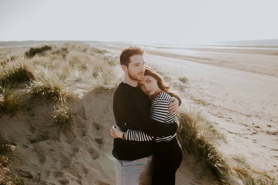 A couple shares an intimate embrace on sandy dunes overlooking Holkham beach in Norfolk