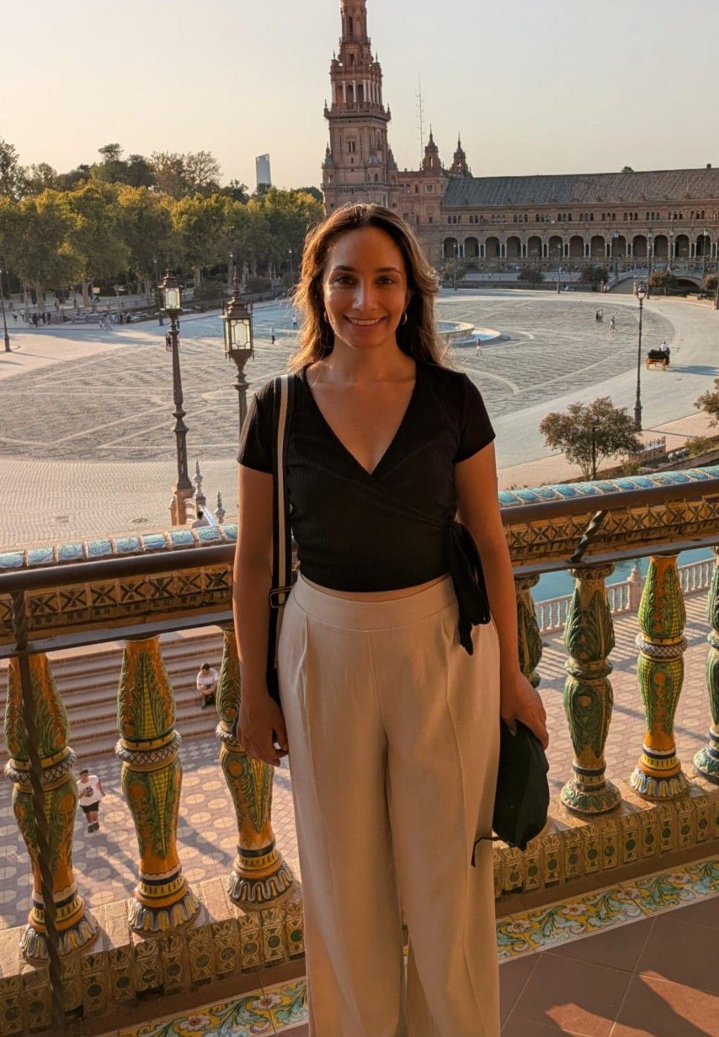 Woman poses on ornate balcony with view of Plaza de España's historic architecture in Seville.