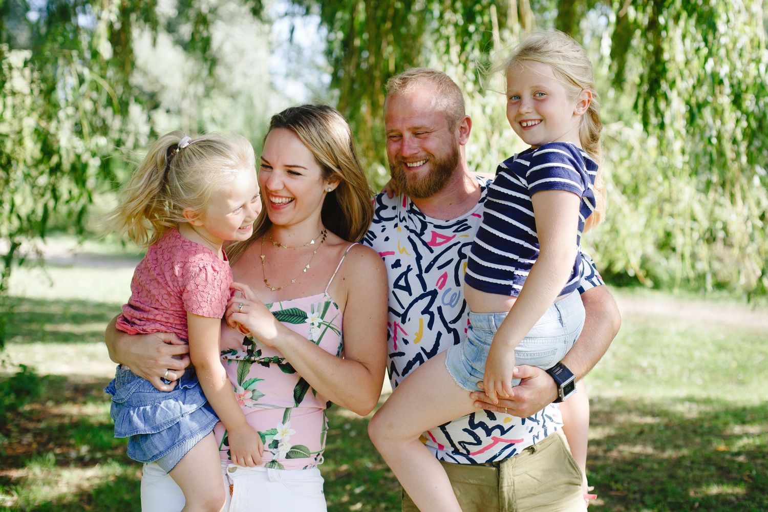 Happy family enjoying a summer day together under a willow tree in a park.