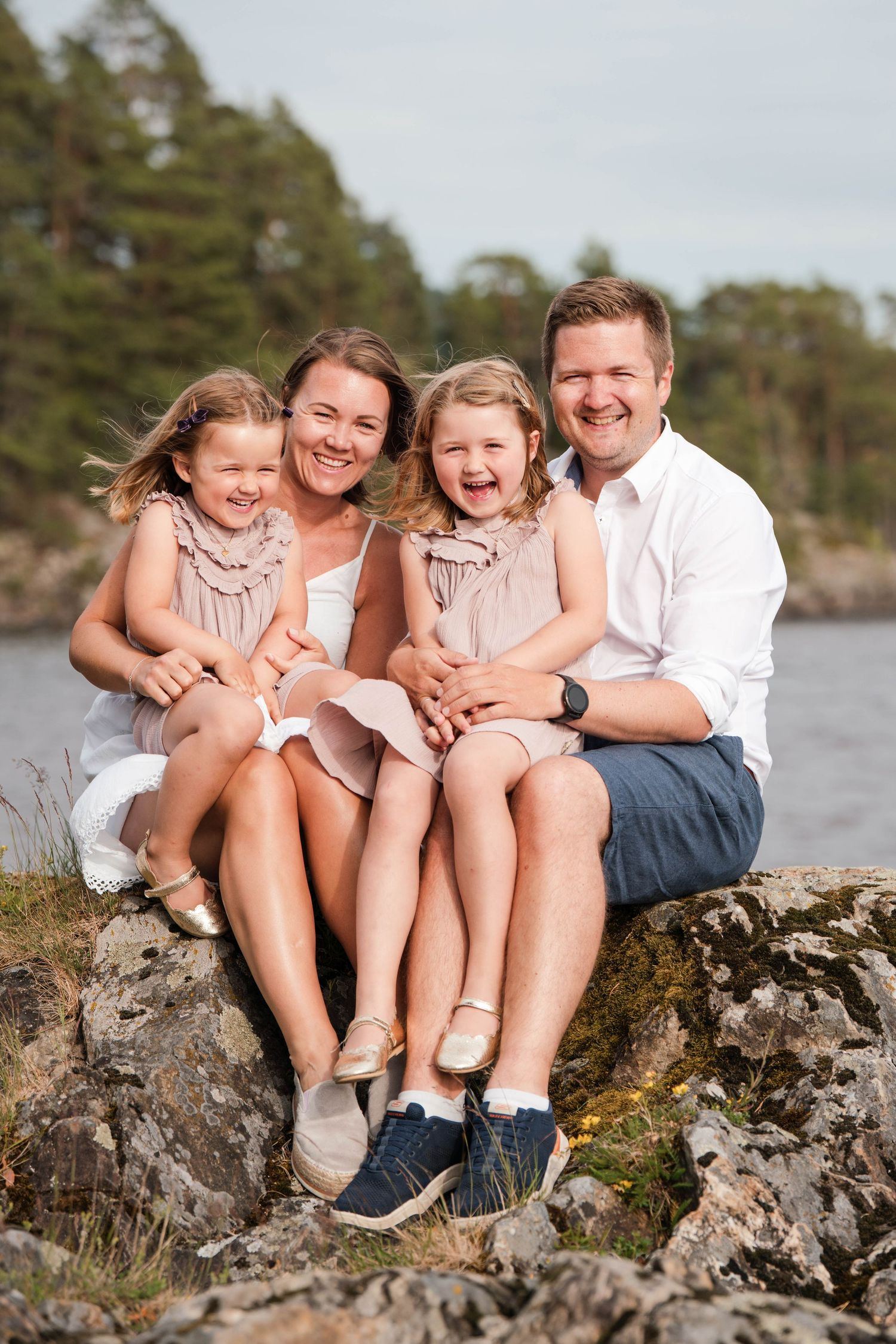 A family sitting together on coastal rocks with matching outfits and joyful expressions.