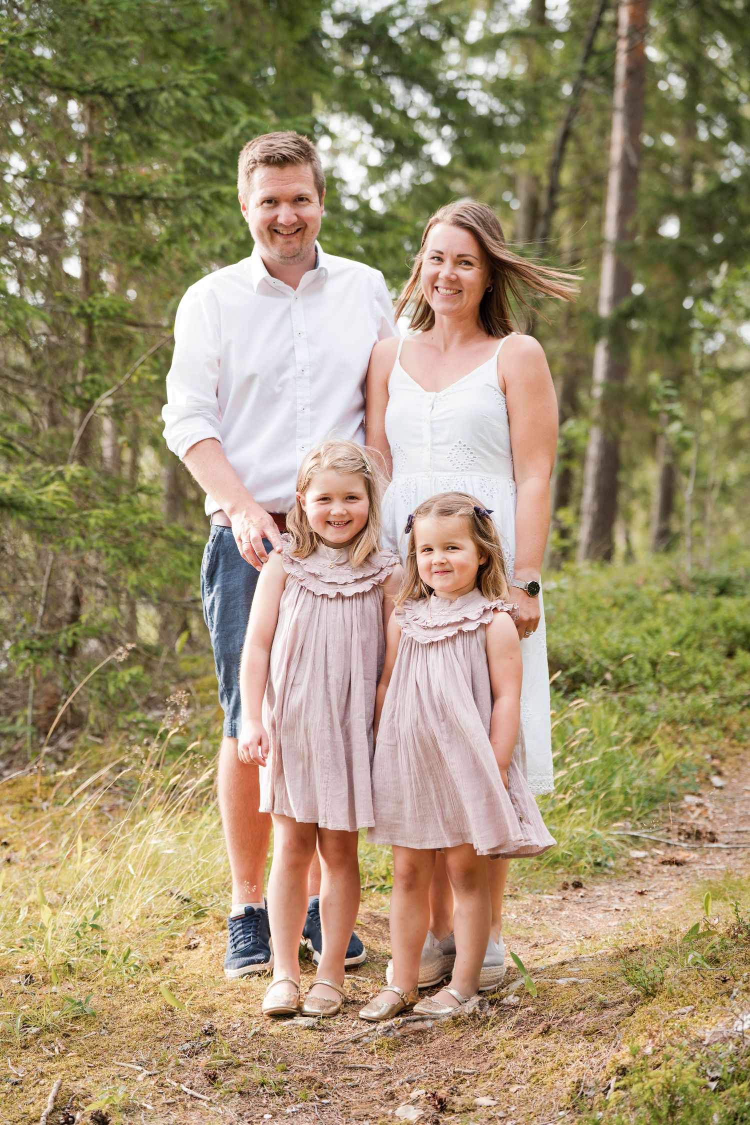 A family of four poses together on a forest trail wearing coordinated white and pink outfits.