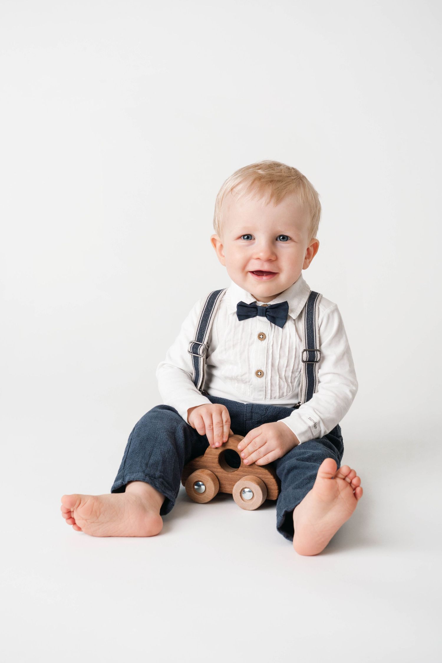 Baby wearing formal bow tie outfit sits and smiles on white background.