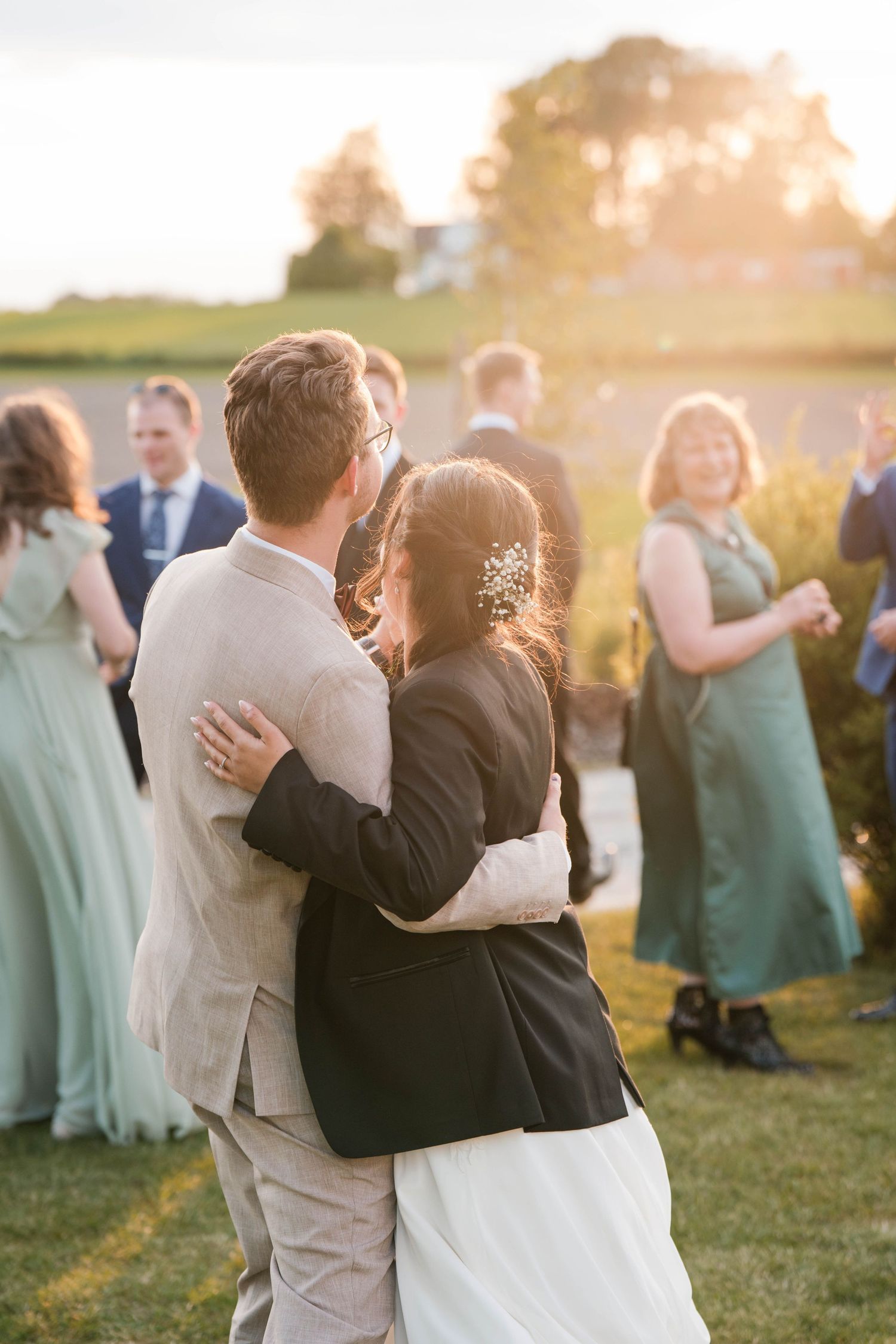 Wedding party embracing during sunset celebration with bridesmaids in sage green dresses.