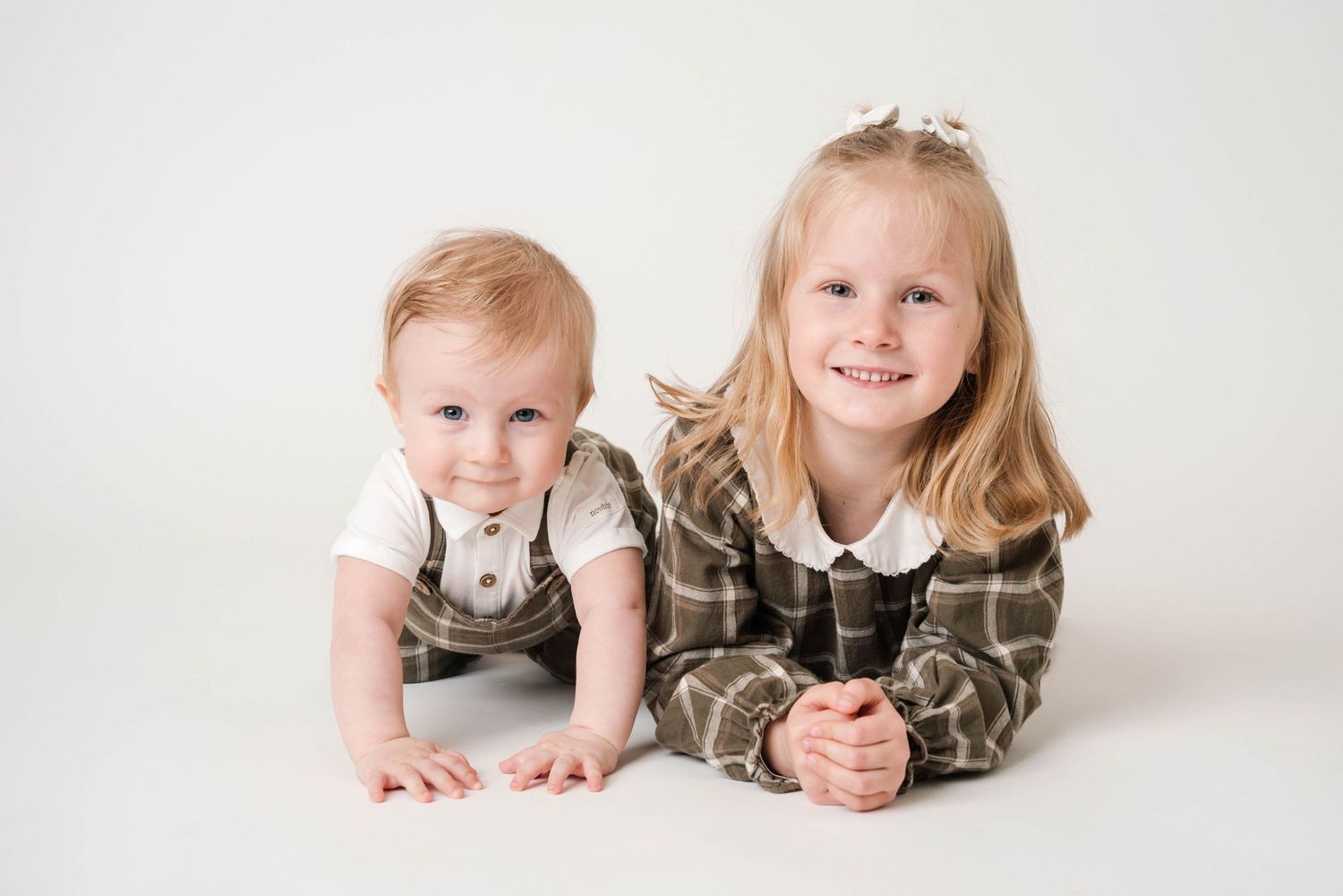 Children lying on white studio floor in matching outfits.