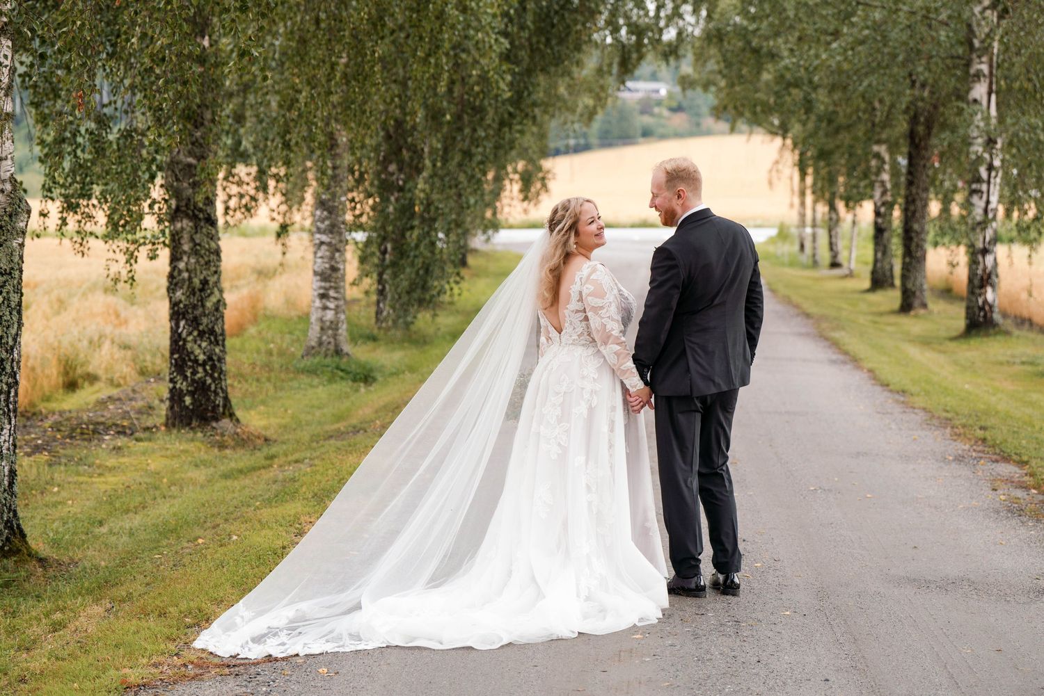 Wedding couple strolls along tree-lined path during autumn outdoor photo session.