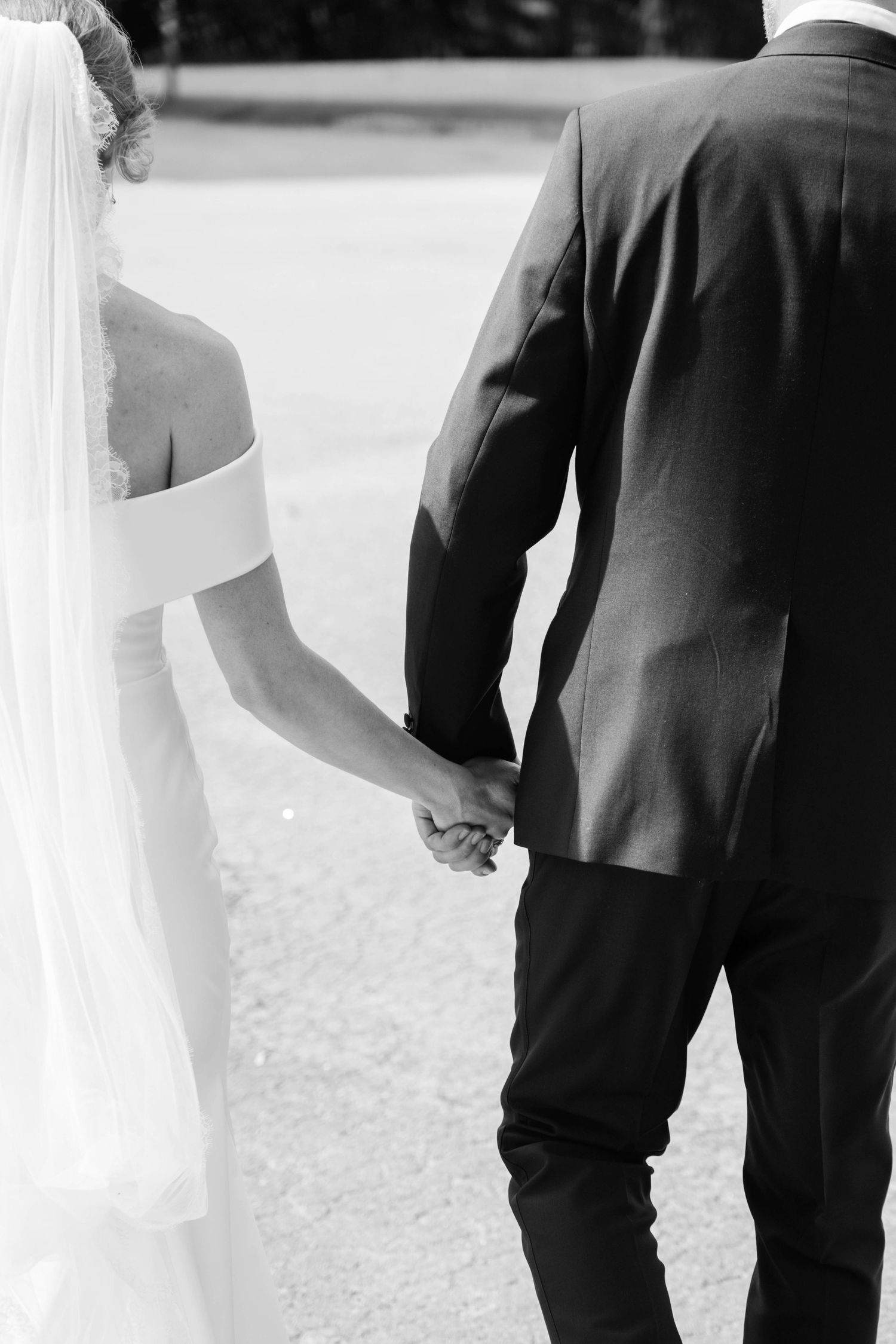 An intimate black and white photo shows a bride and groom holding hands during their ceremony.