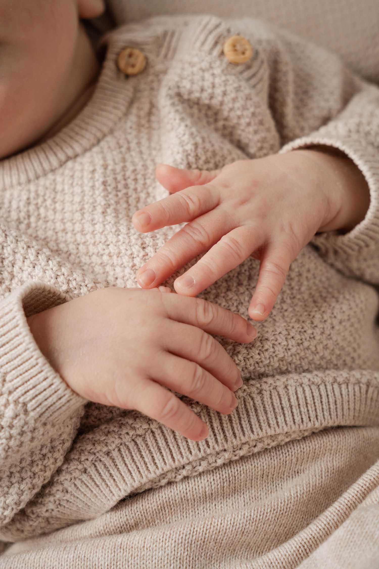 Small baby hands gently touch and explore a soft beige knitted sweater texture.