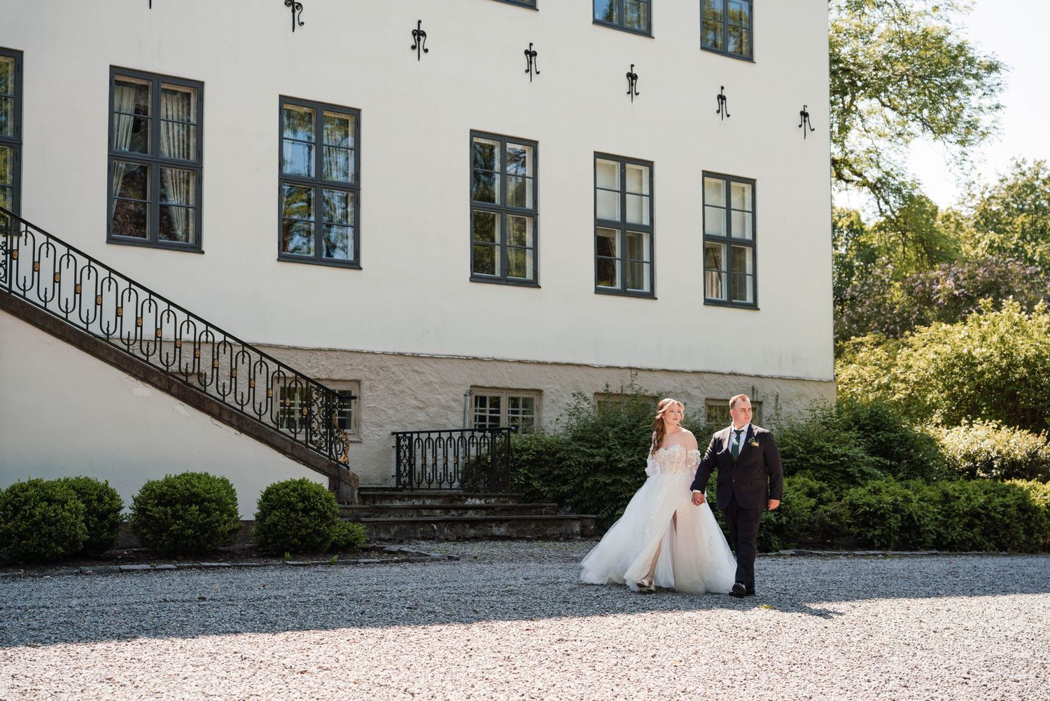 Wedding couple poses in front of elegant white mansion with stone steps.