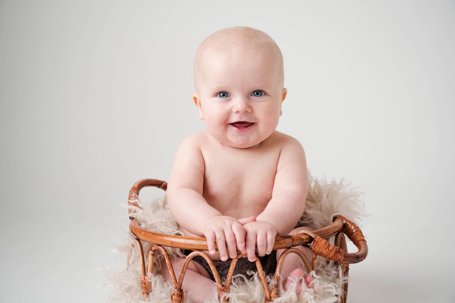 Baby sitting in wooden bowl against white studio background.