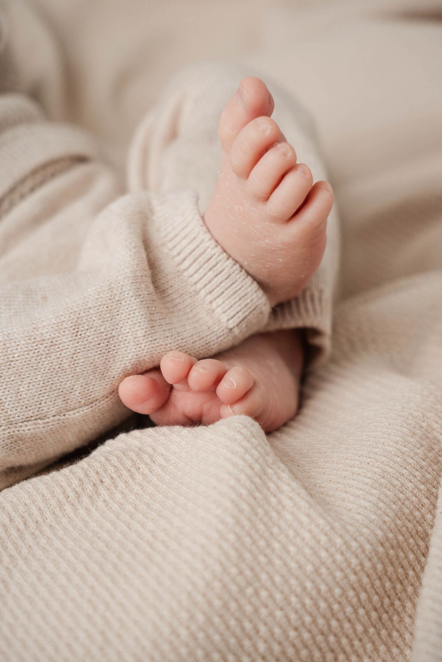 Close up view of tiny baby toes and feet resting on soft beige knitted blanket.