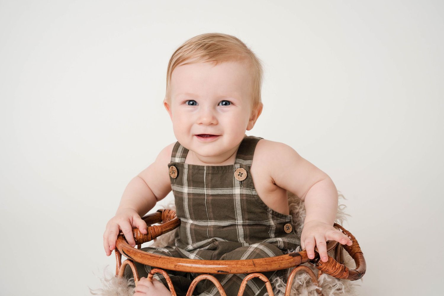 A baby in a gray striped romper sits in a wooden bowl with a joyful expression.