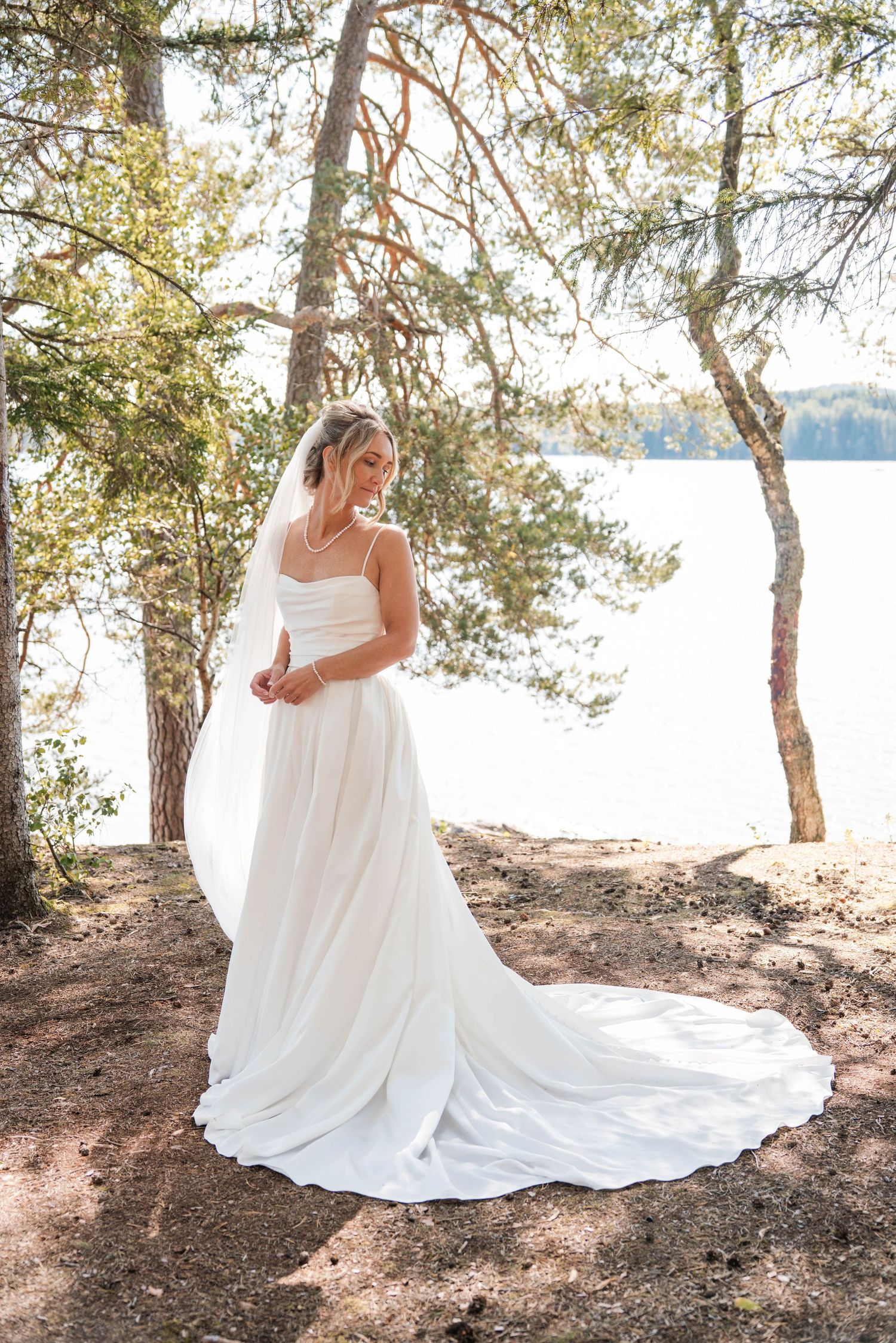 A flowing white wedding dress photographed against a lakeside forest backdrop.