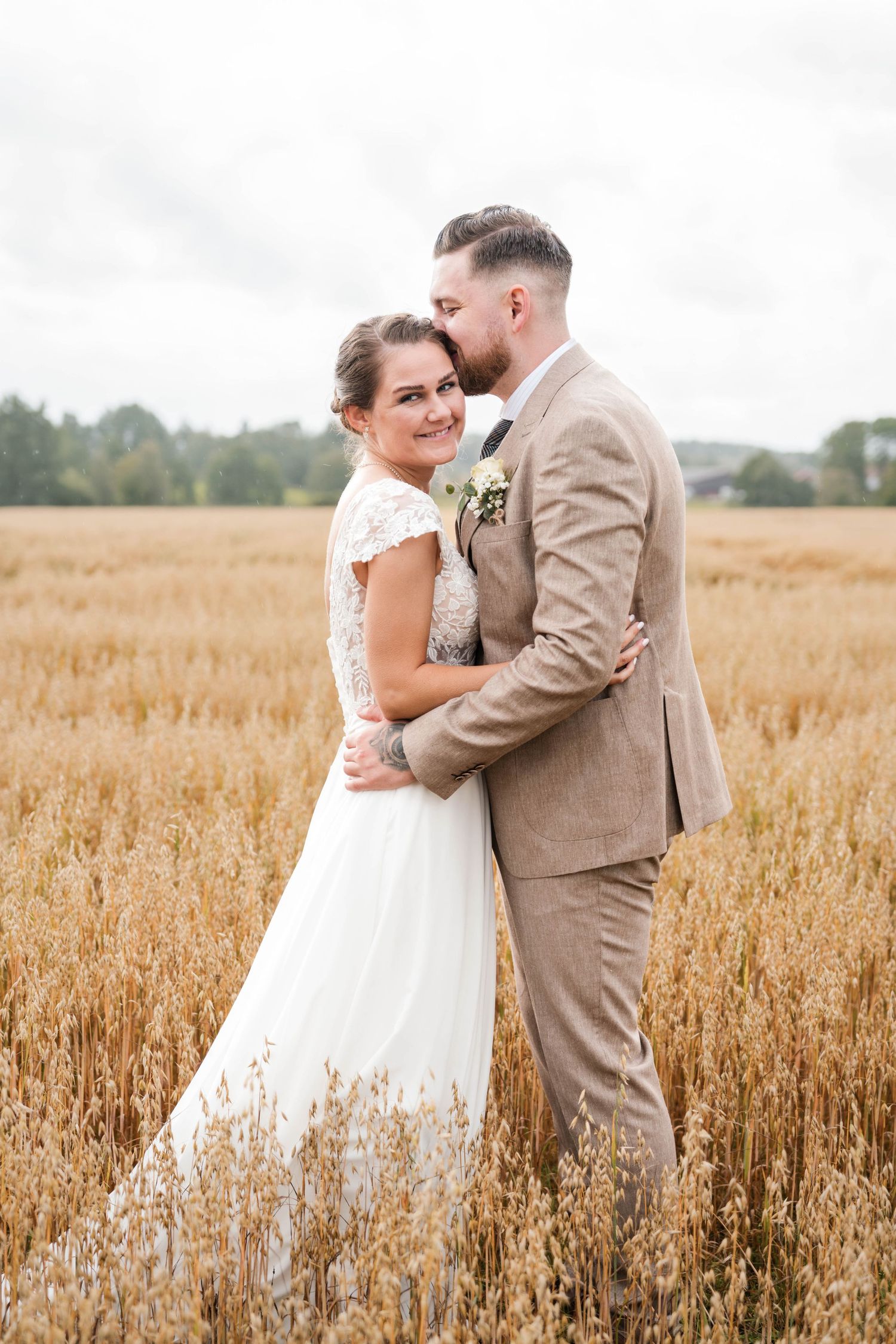 Romantic wedding couple embraces in a golden wheat field wearing beige suit and white dress.