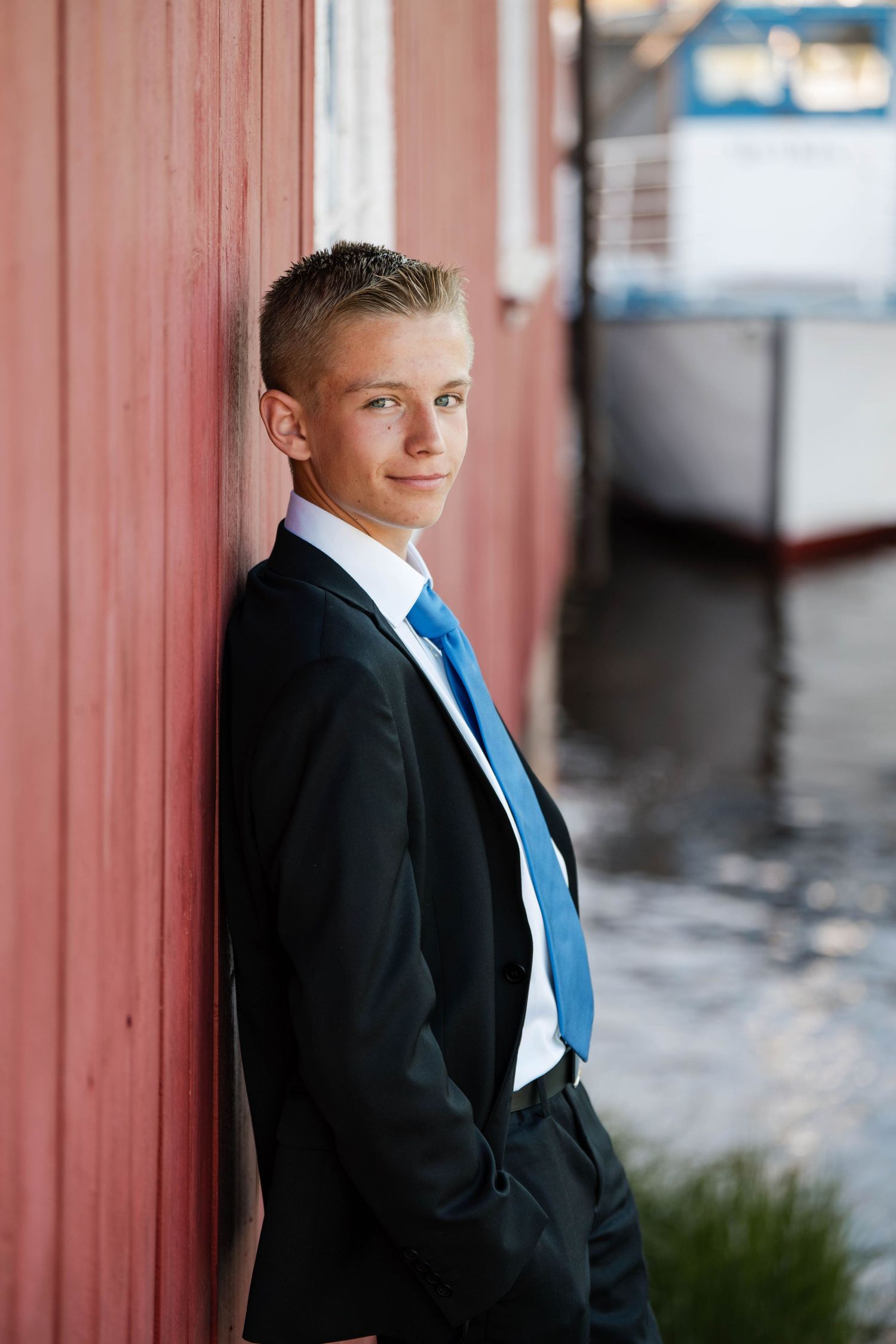 Young boy in formal suit poses against red wall in dramatic lighting.