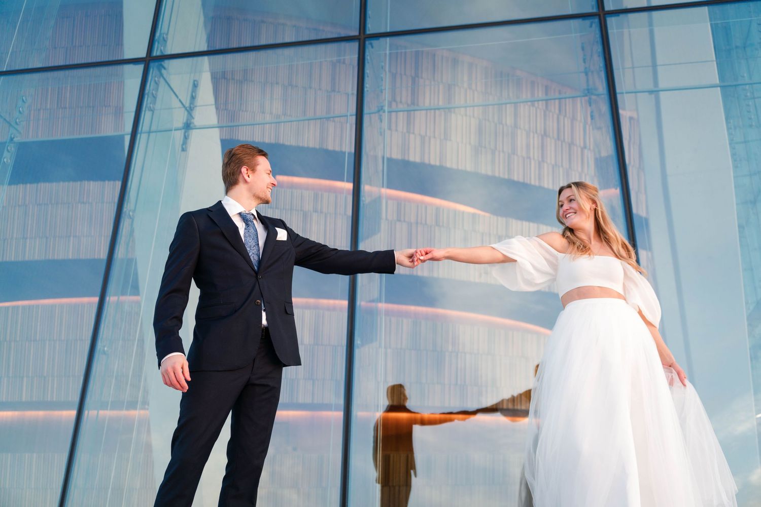 A couple in wedding attire dances gracefully in front of a modern glass building facade.