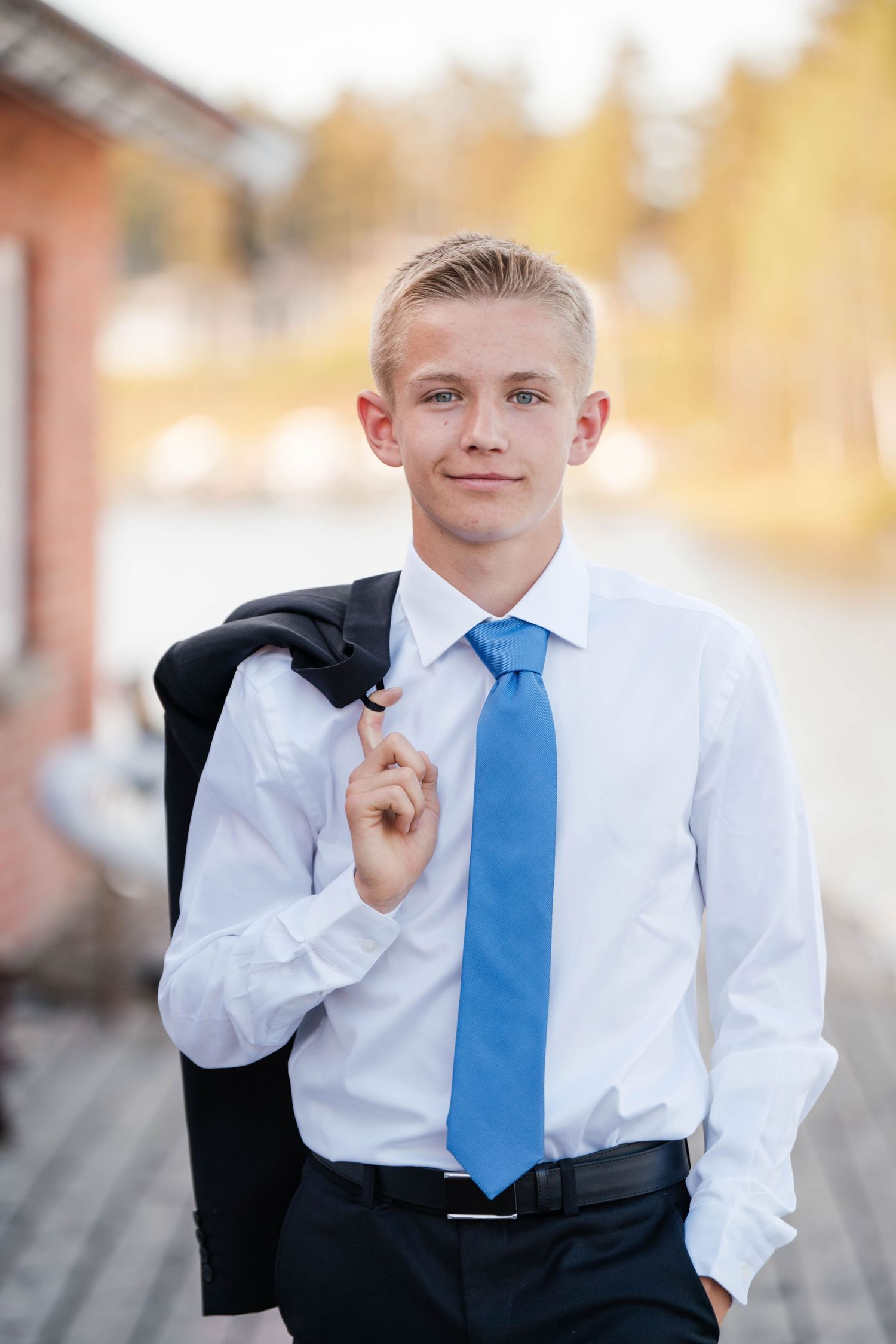A casual formal portrait showing a person holding a suit jacket over their shoulder.