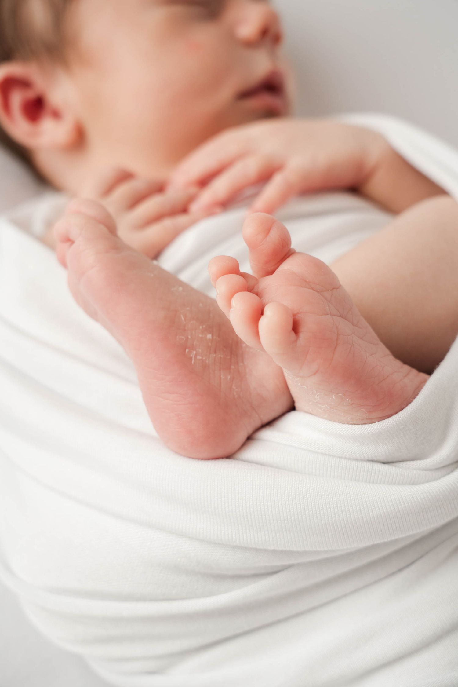 Close-up series of tiny baby feet wrapped in soft white blankets showing different angles of delicate newborn toes.