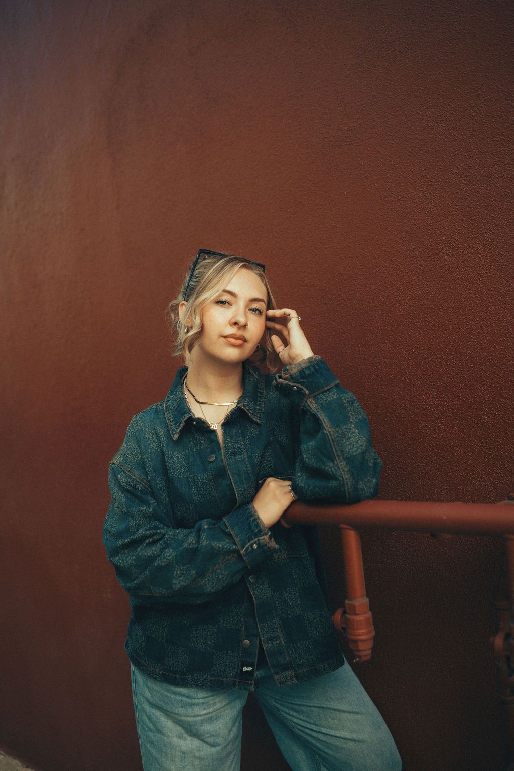 A person in a teal denim jacket and jeans poses thoughtfully against a dark brown background in a vintage style portrait.