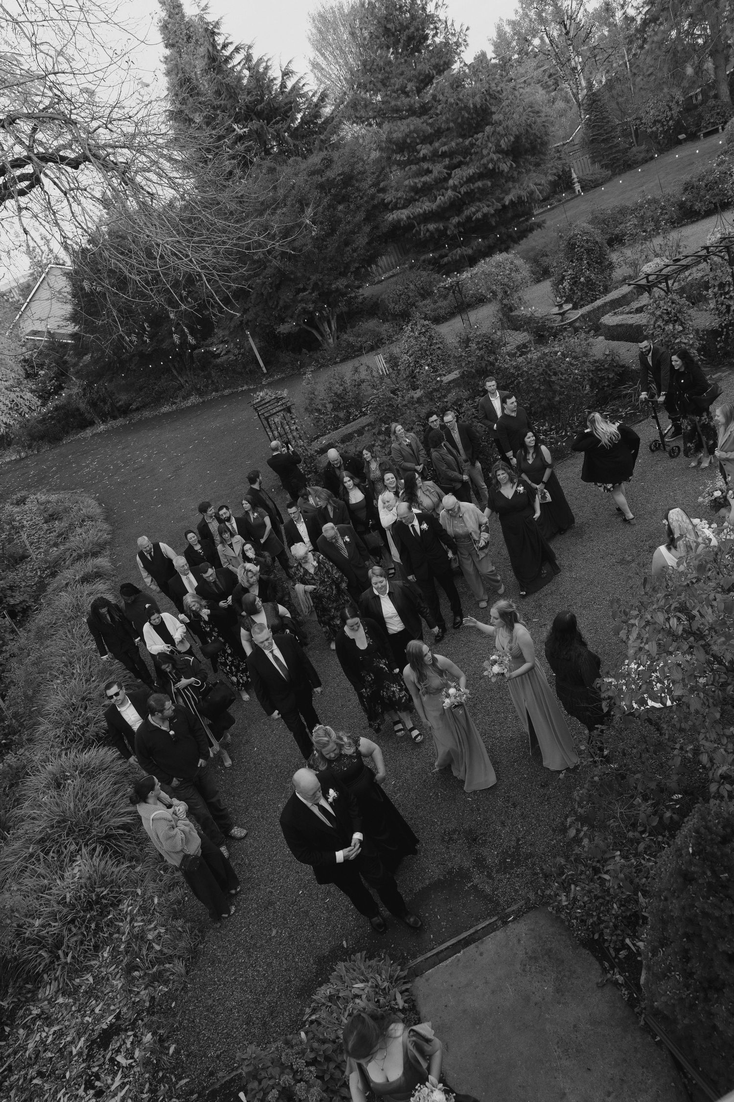 Aerial black and white view of a formal gathering on a garden path surrounded by sloping landscaped grounds.