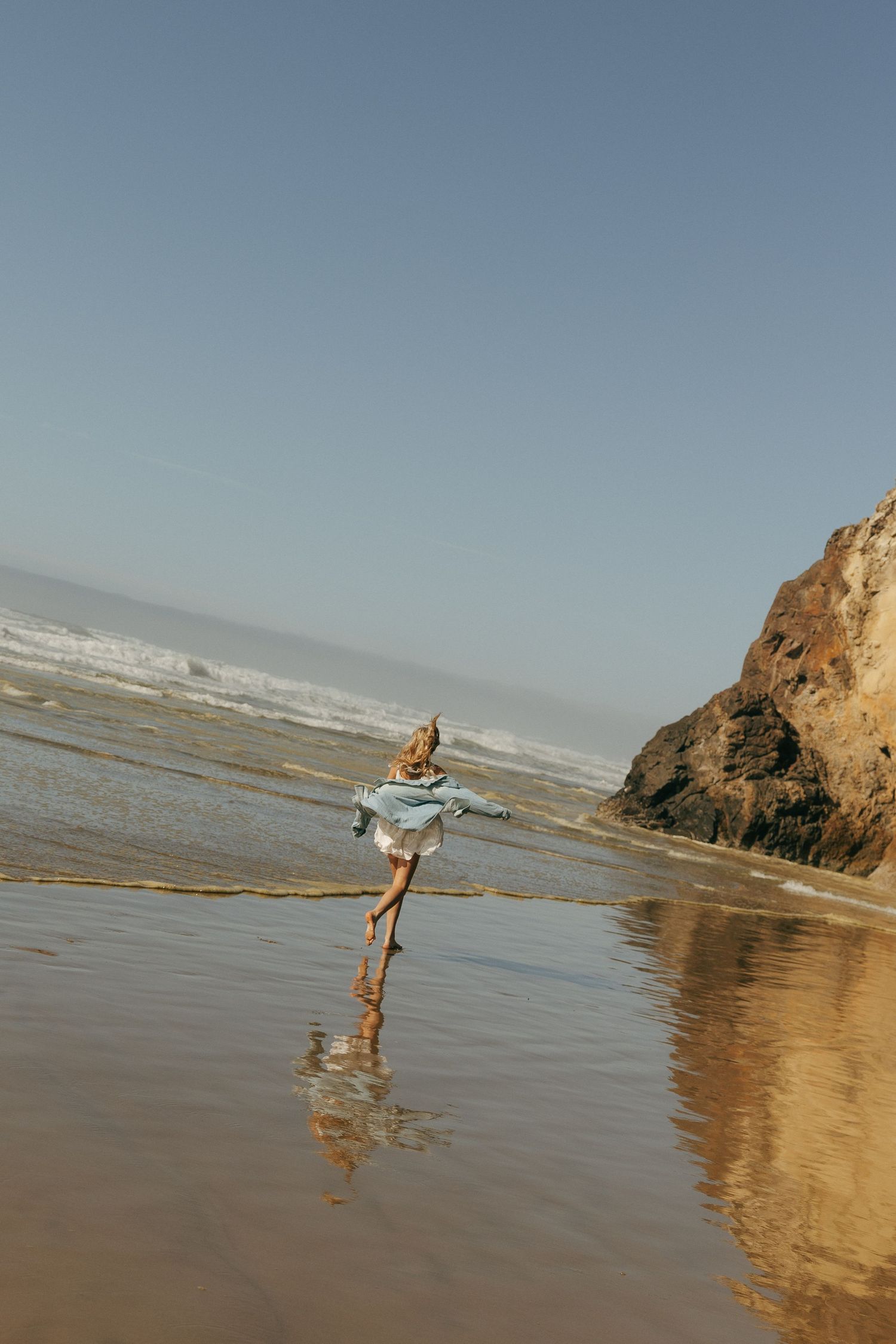 Person walking along shoreline near coastal cliffs during sunset.