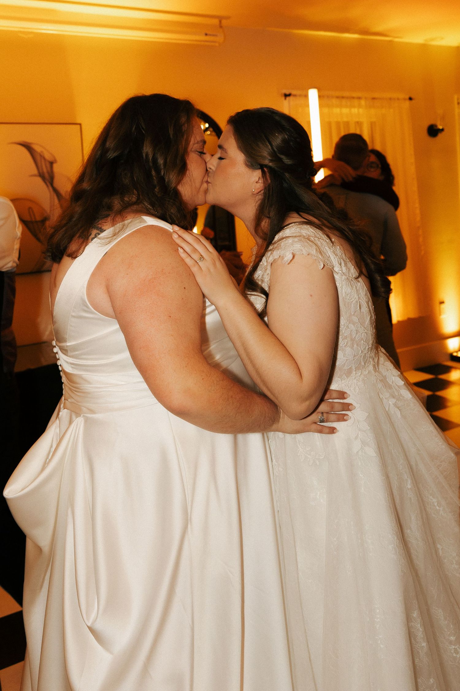 Two brides in white wedding dresses share an intimate dance moment at their wedding reception.