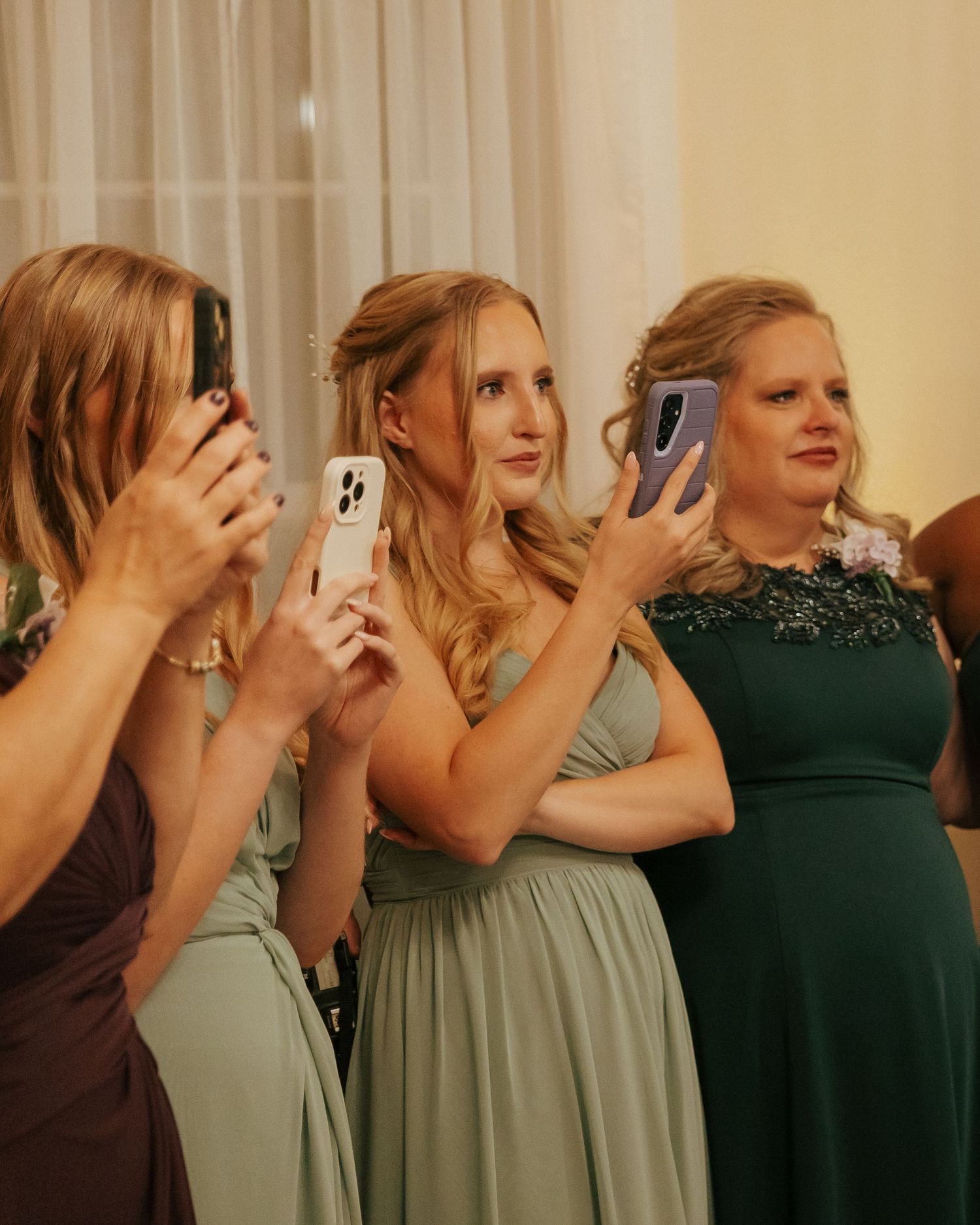 Group wearing sage green dresses holding up phones to take photos together.