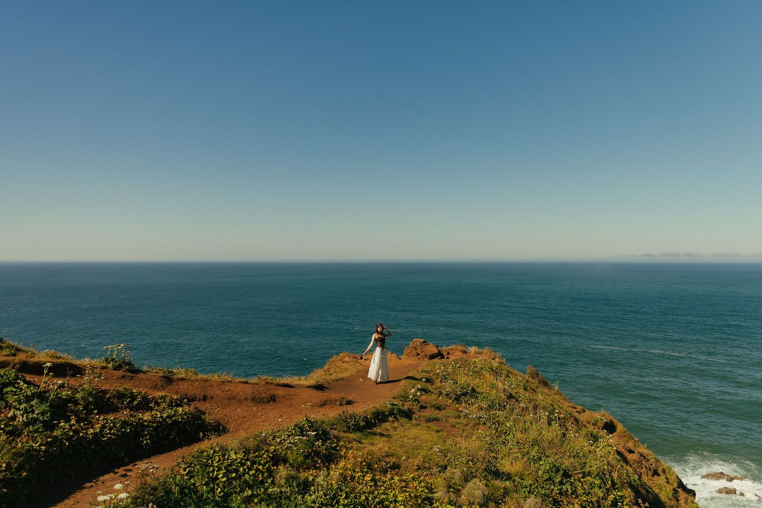 Panoramic view of rugged coastline with lighthouse perched on grassy cliff overlooking ocean.