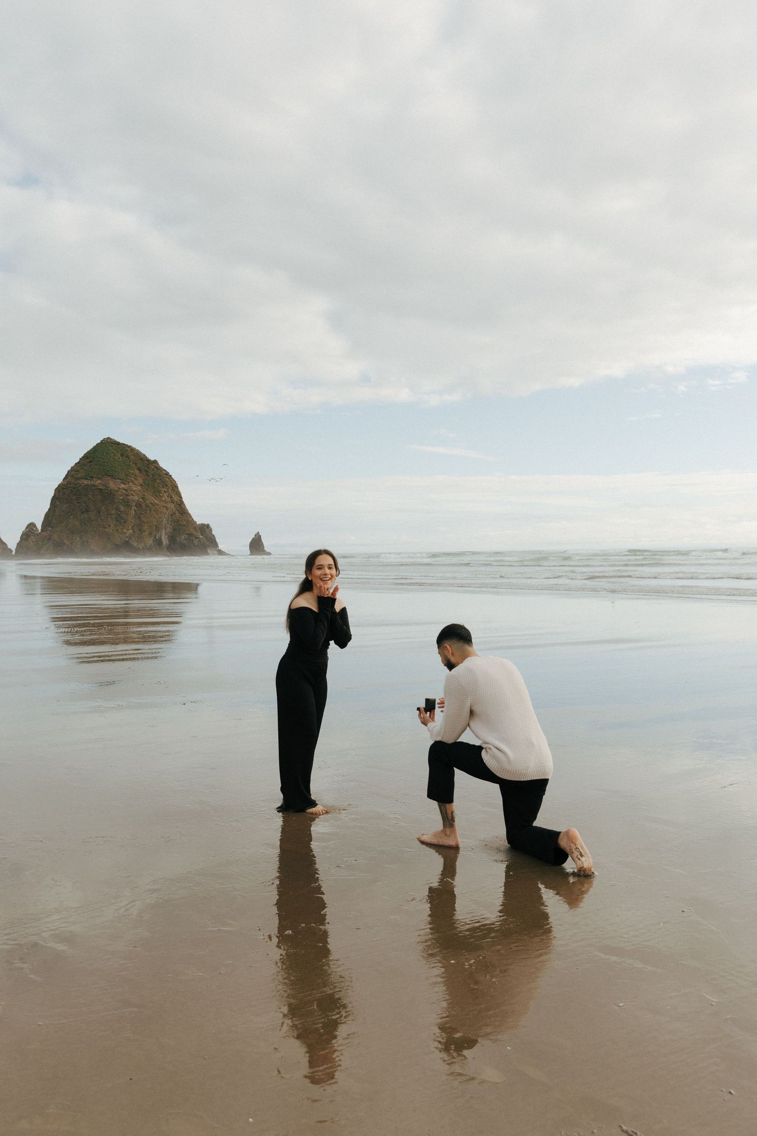 Marriage proposal scene on beach with Haystack Rock at Cannon Beach in background.