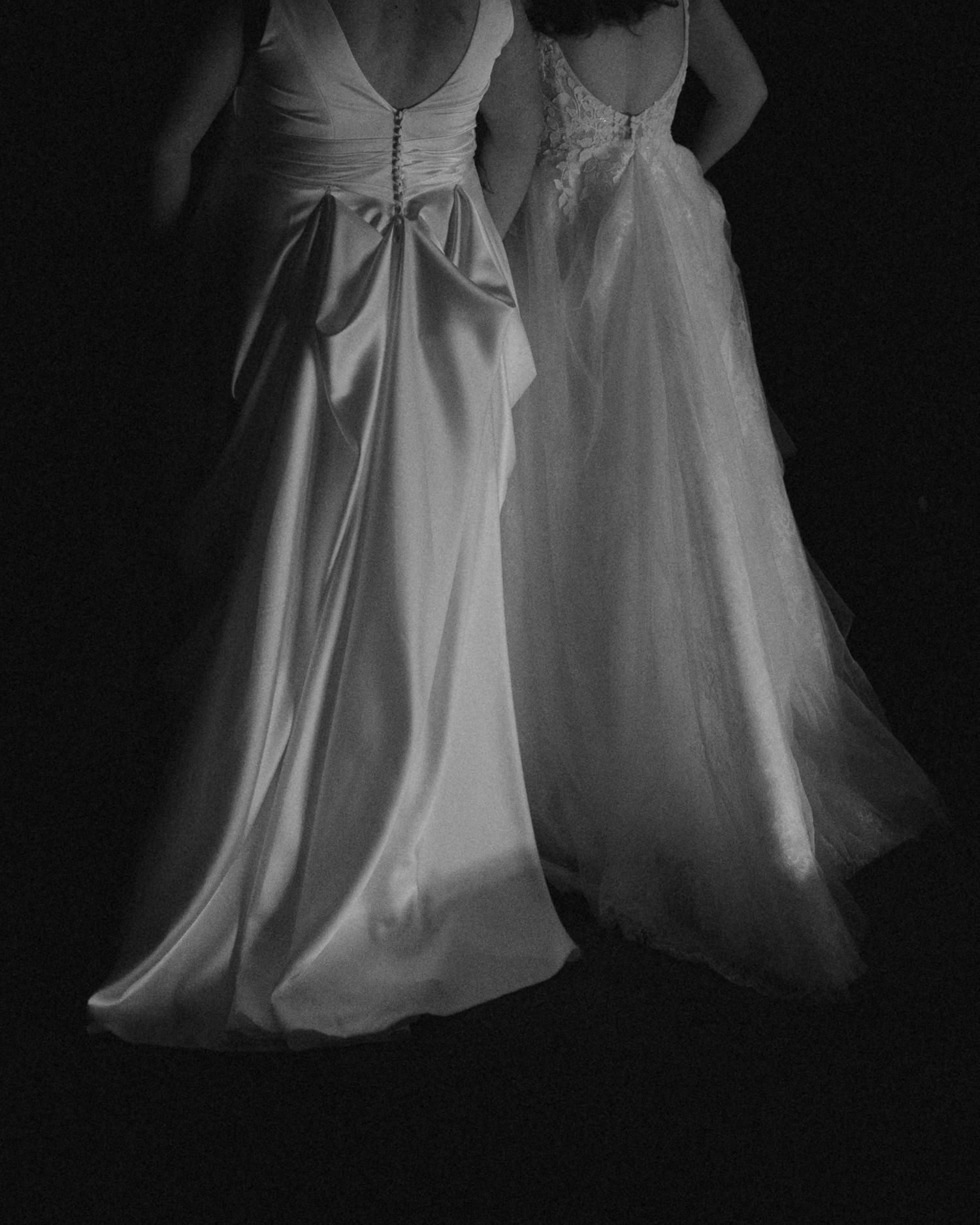 Two elegant white wedding dresses photographed in black and white, showing intricate back details.