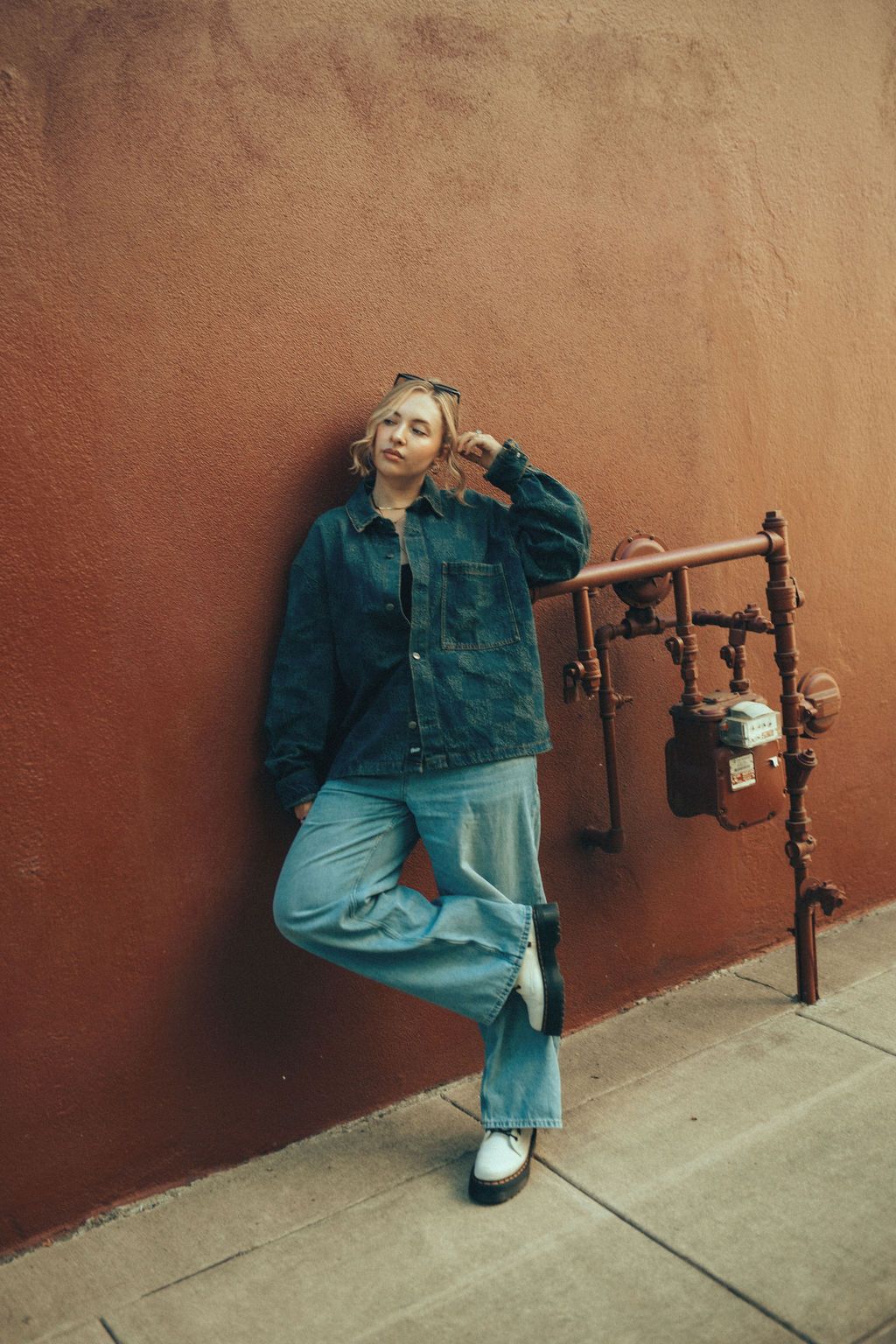 Casual denim style shoot with industrial pipes and terracotta wall backdrop.
