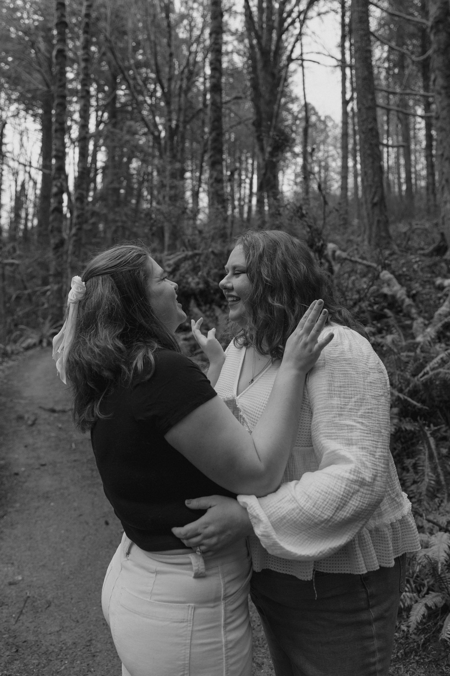 Black and white photo of two women embracing on forest path.