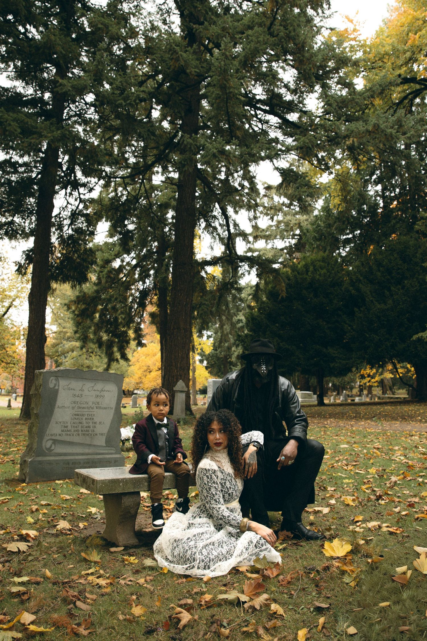 Group poses among gravestones in an autumn cemetery with scattered yellow leaves.