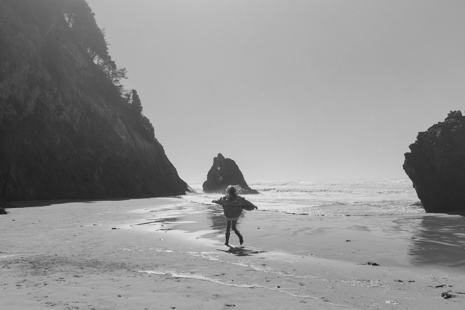 Black and white beach scene with dramatic rocky cliffs and coastal landscape.