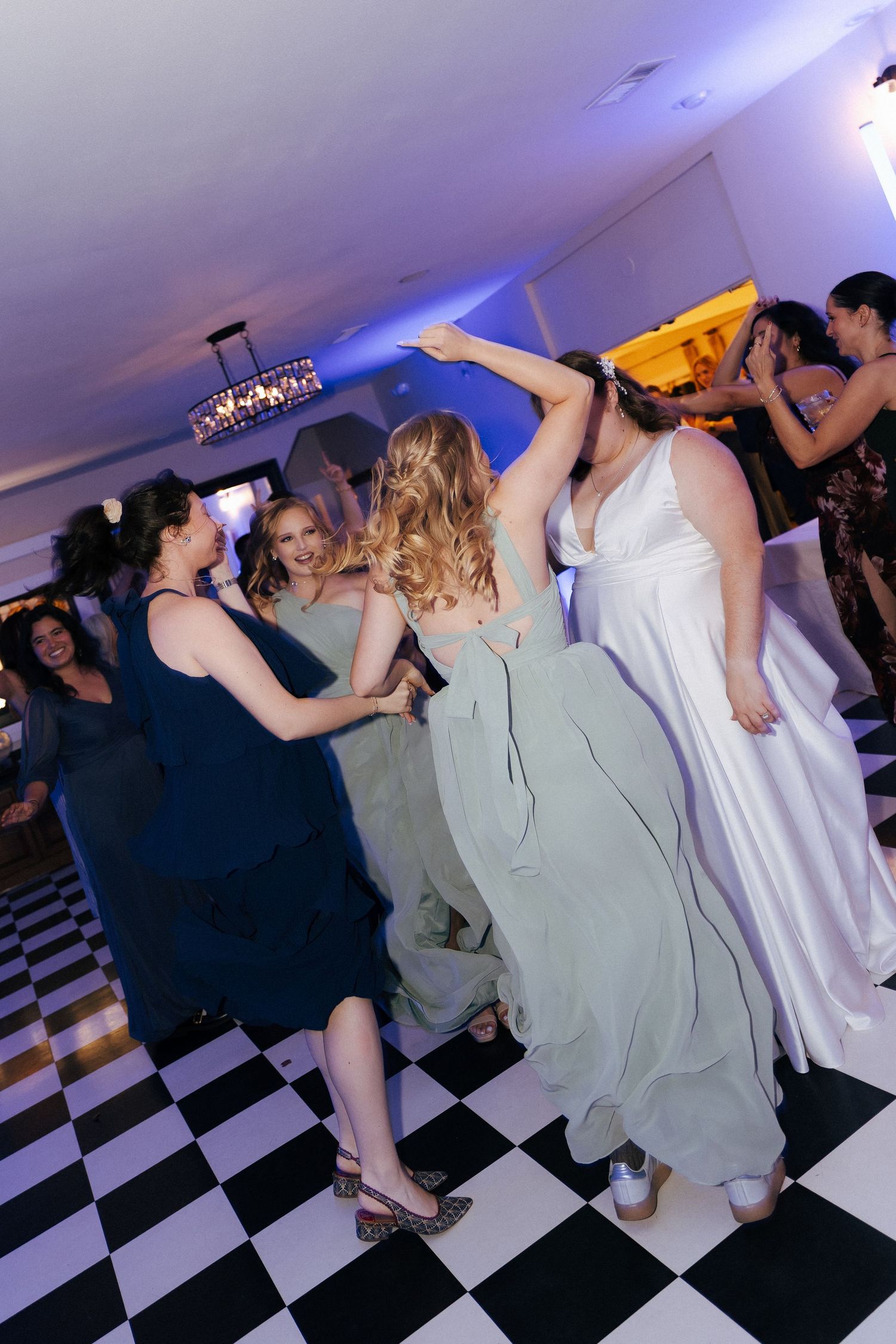 Wedding party guests dancing on a black and white checkered dance floor under blue lighting at a reception.