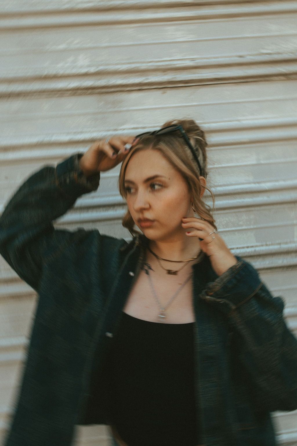 Fashion model in dark denim jacket poses expressively against white industrial backdrop.