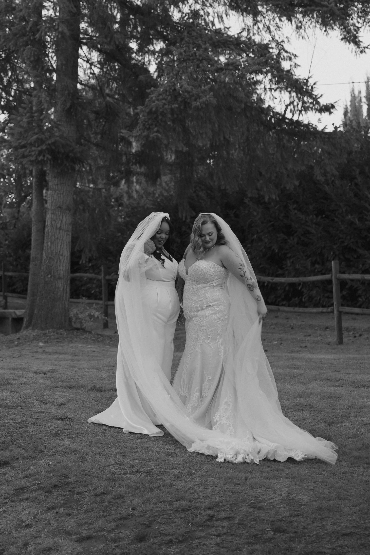 Two figures in flowing white dresses sitting together on grass in an ethereal outdoor setting.