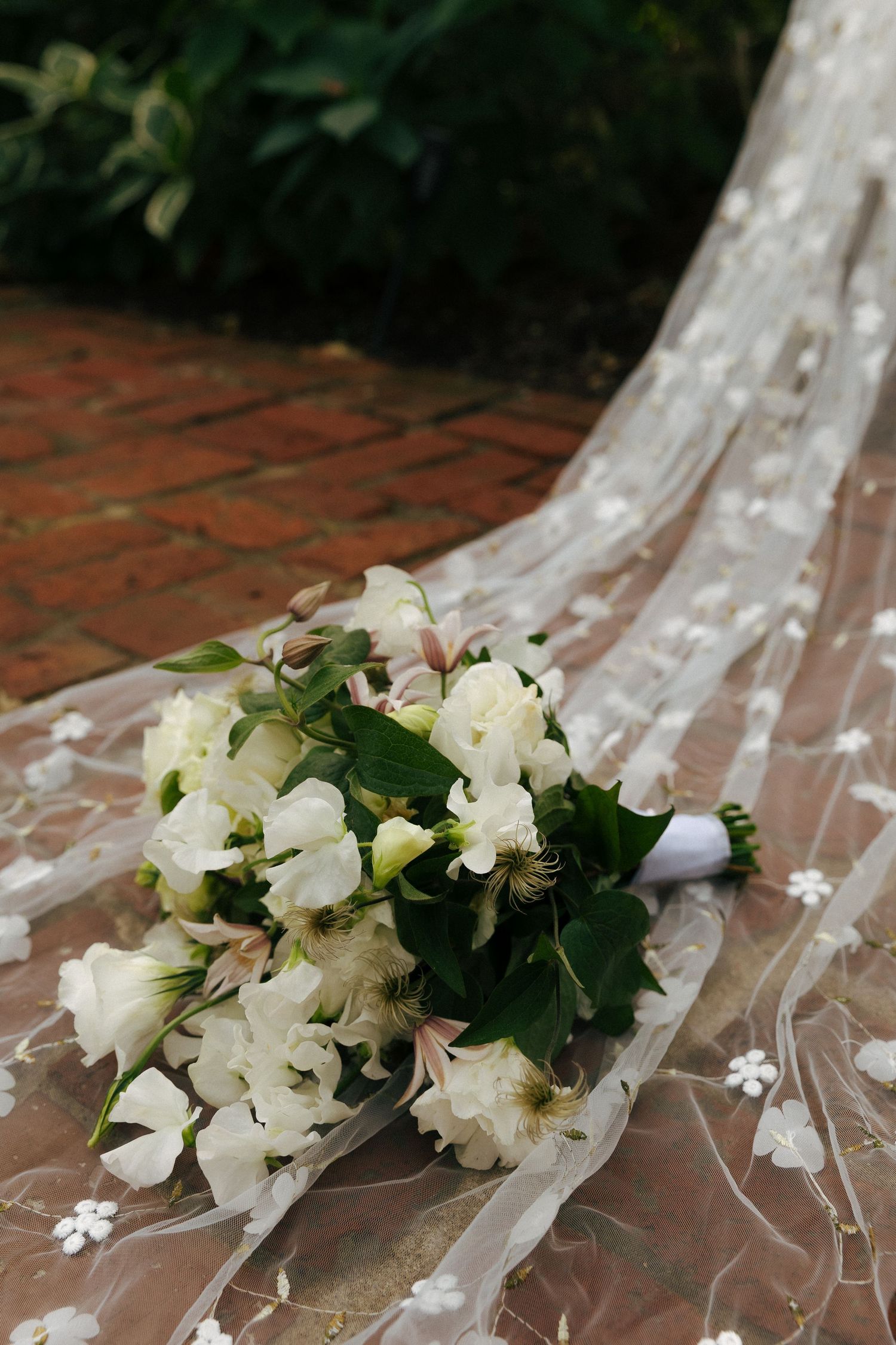 White flowers and greenery lay elegantly on flowing sheer fabric with delicate floral details.