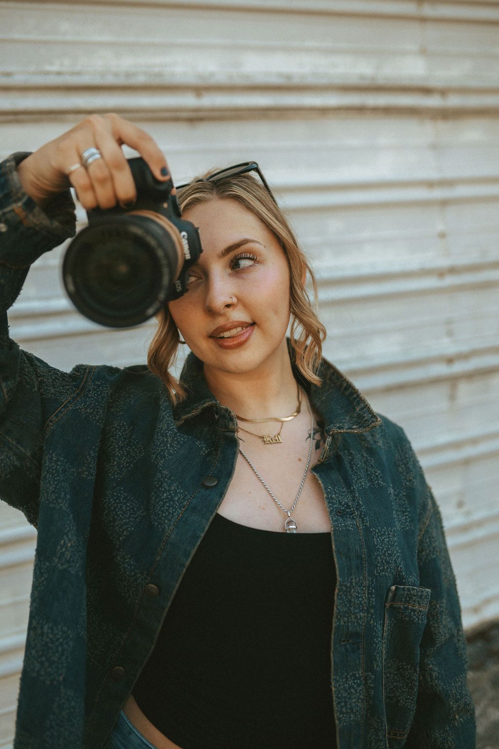 Girl in denim jacket holding professional camera while taking photos outdoors.