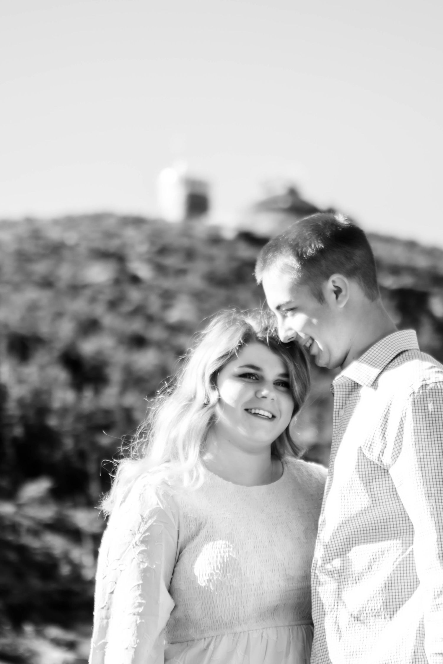 A couple shares tender moments in bright sunlight against a desert landscape backdrop.