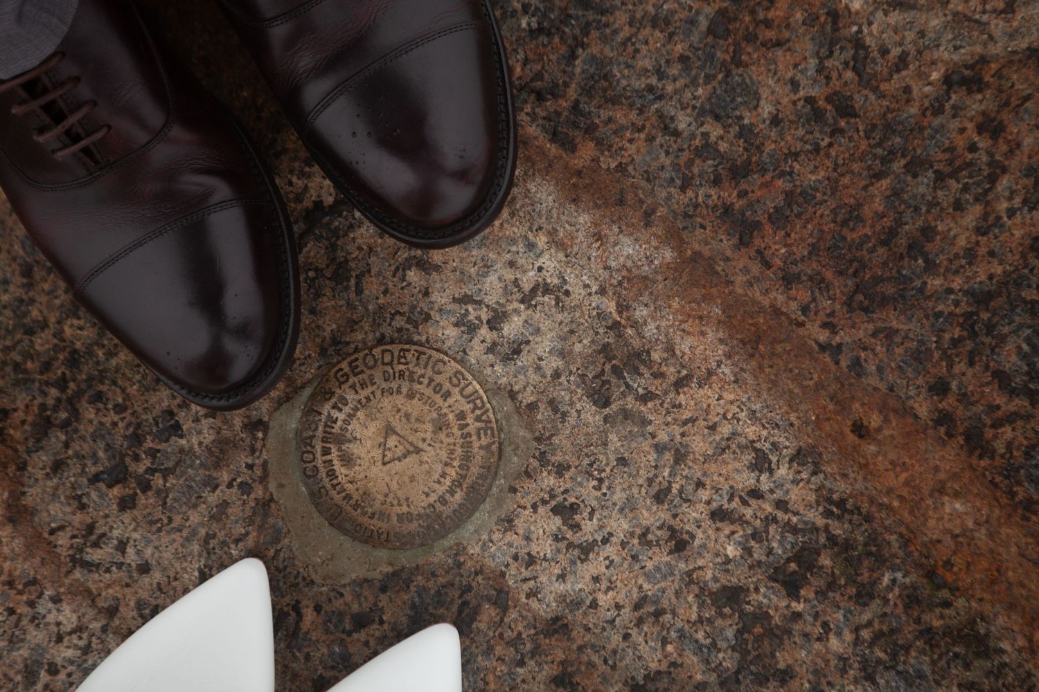 Wedding shoes and rings arranged on textured stone background.