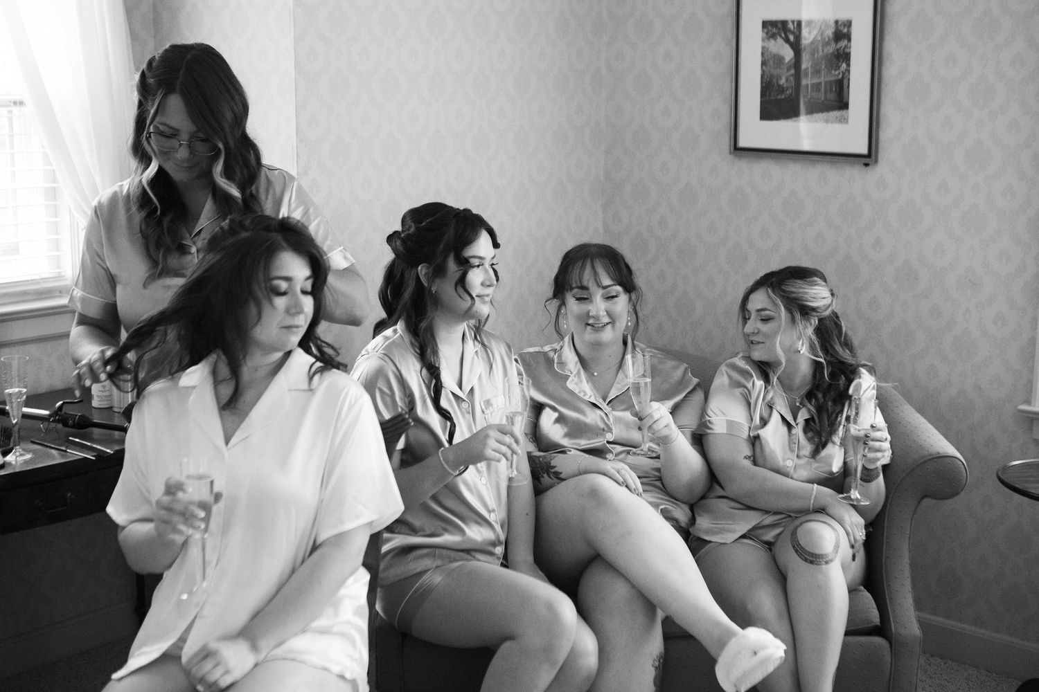 Black and white photo of bridal party getting ready together in a cozy room.