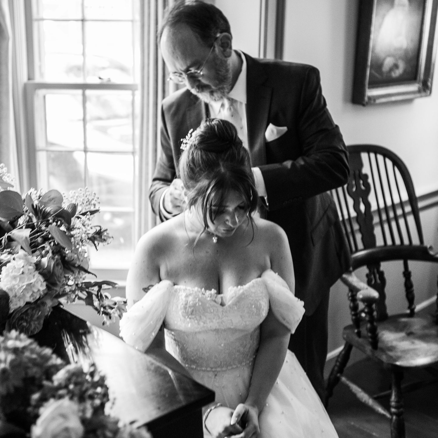 A wedding dress being adjusted in an elegant indoor setting with natural window light.