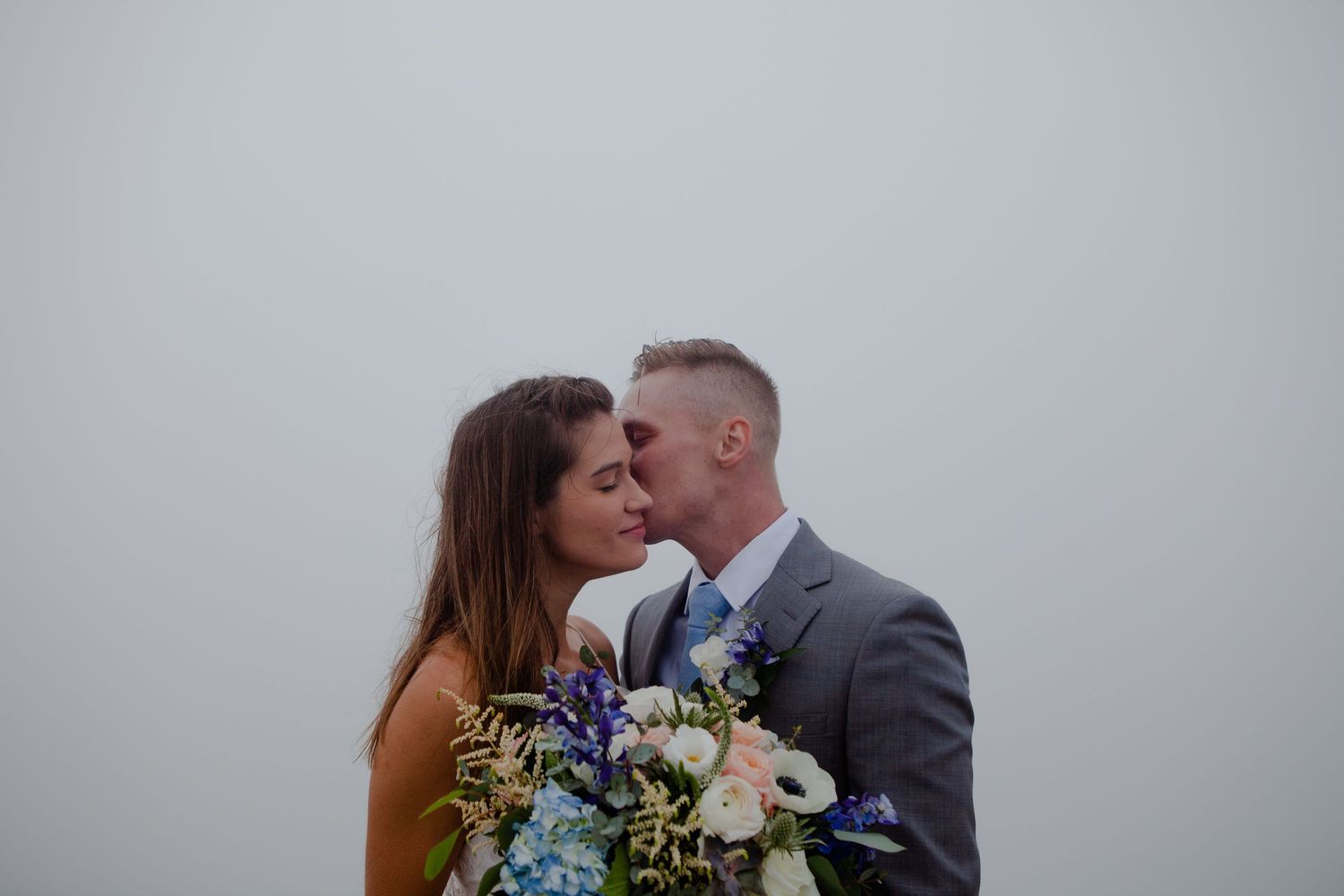 A couple embraces against a misty mountain backdrop during their wedding portraits.
