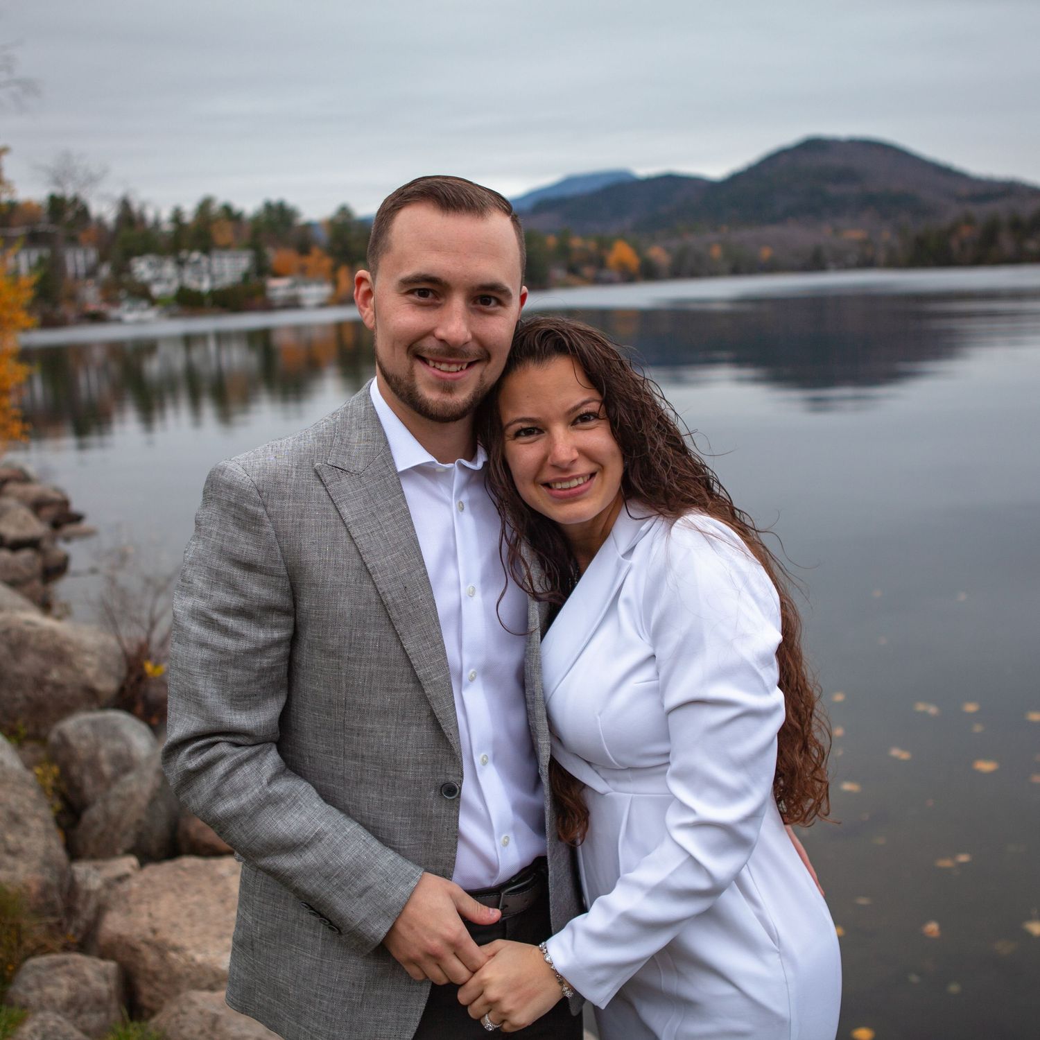 Couple poses for engagement photos by a serene mountain lake during fall.