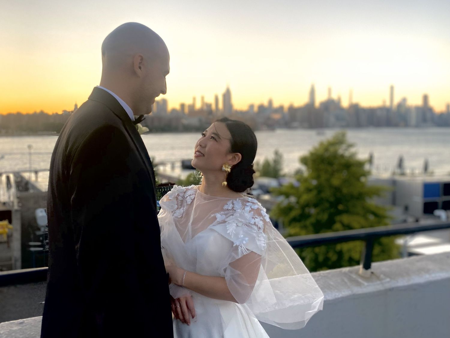 A couple embraces against a city skyline backdrop at sunset.