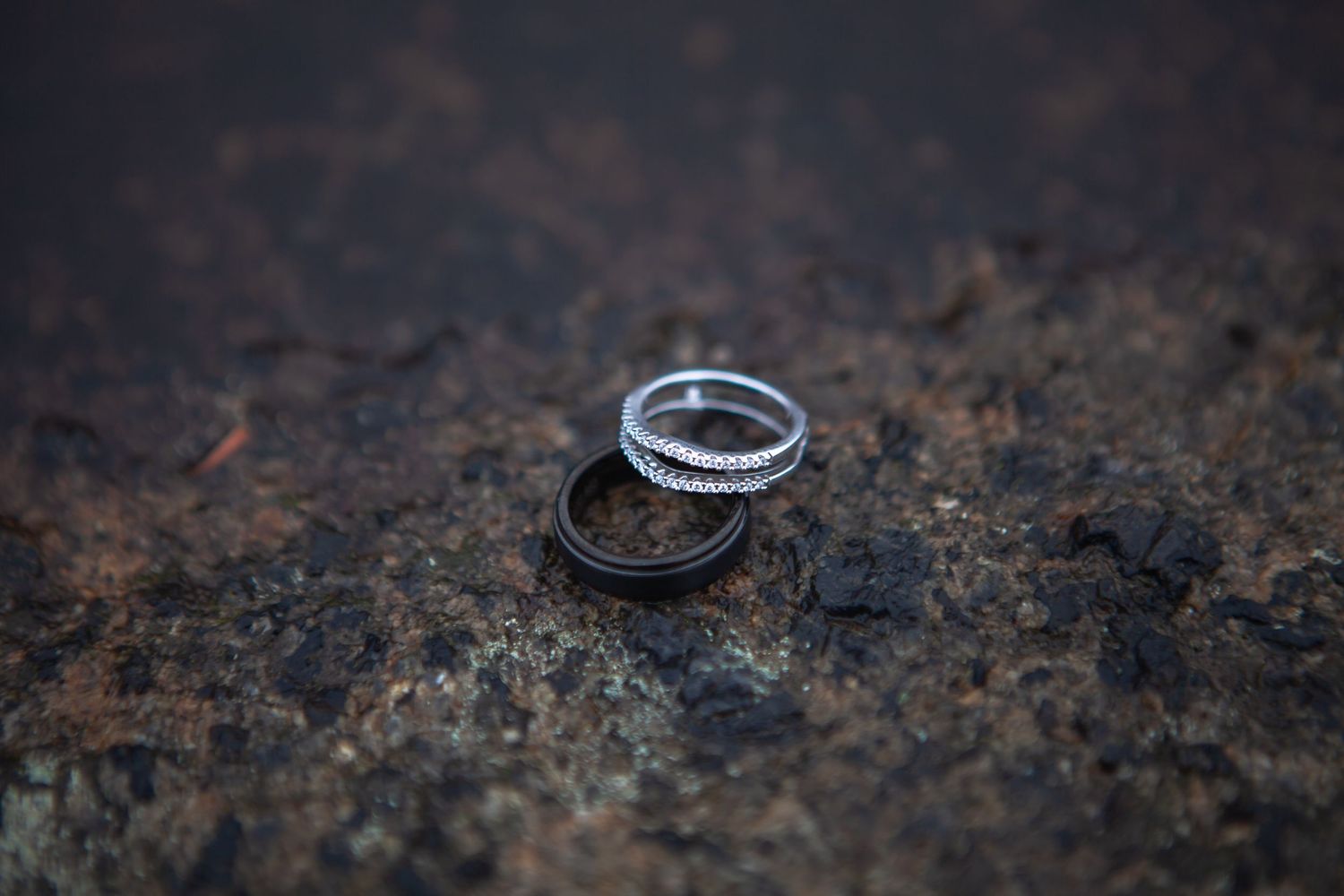 Wedding rings photographed in dramatic lighting on a dark textured surface.