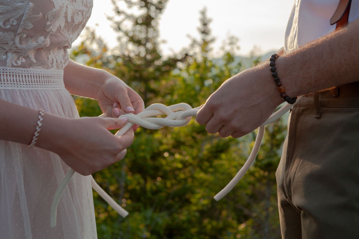 Couple shares an intimate moment during sunset in front of mountain backdrop with white floral bouquet.