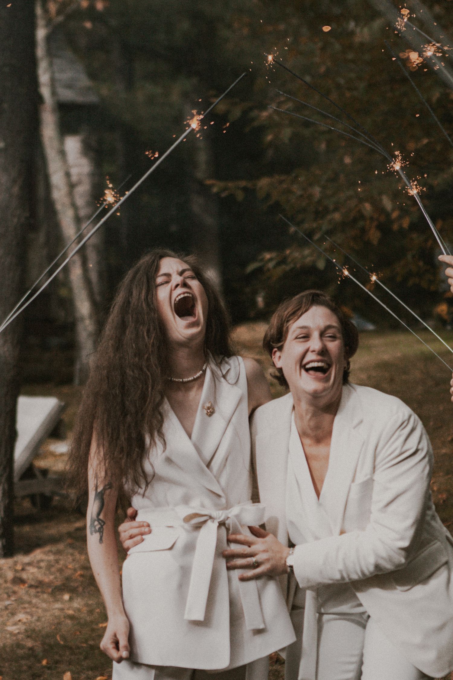 People in white outfits laugh joyfully while holding sparklers outdoors.