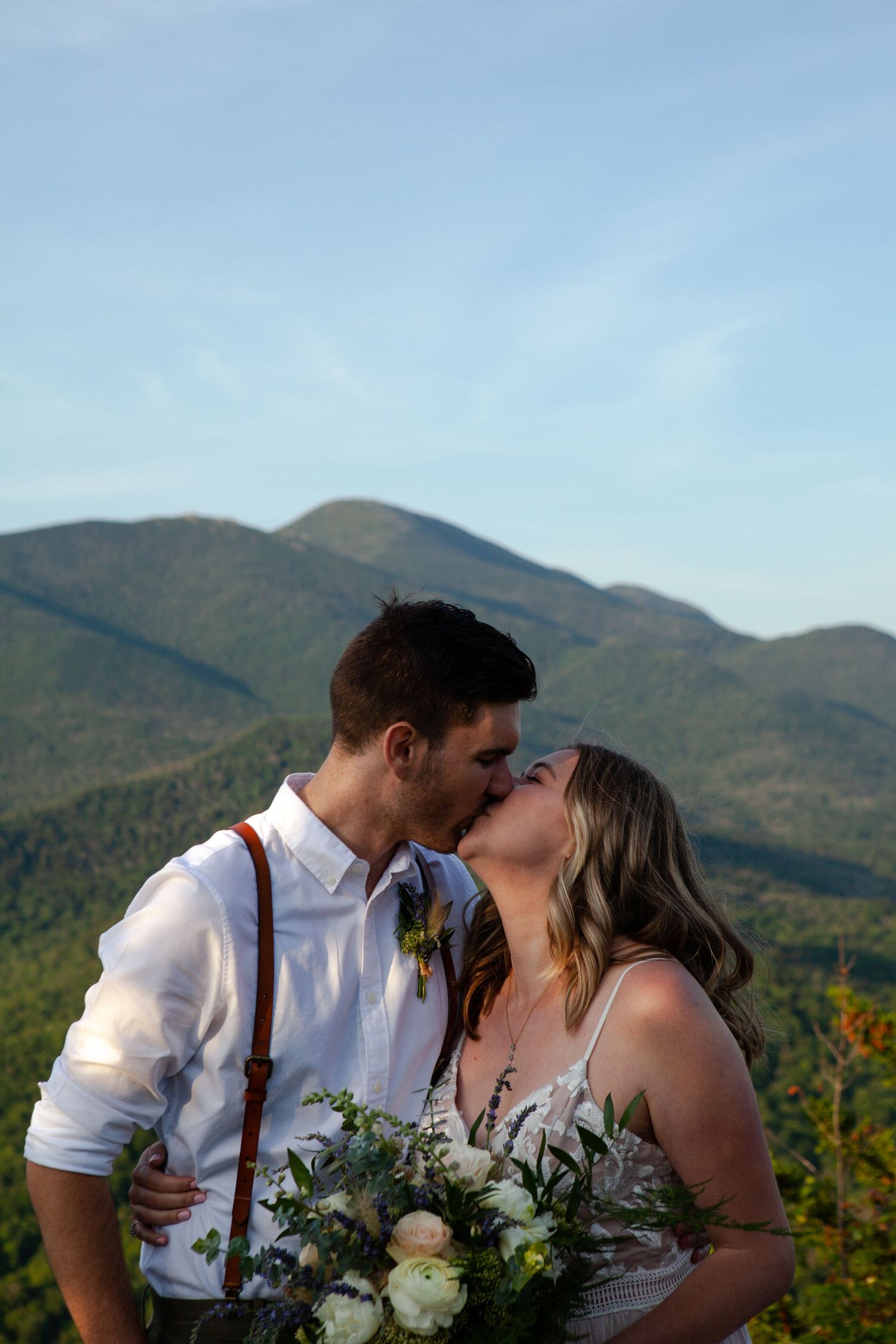A couple embraces with mountain peaks and autumn foliage creating a scenic backdrop.